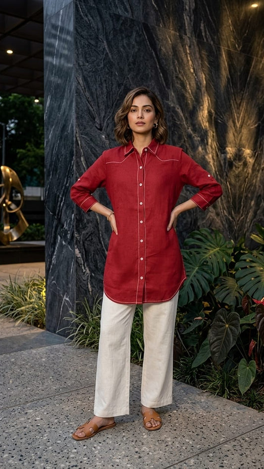 Woman in a red shirt and white pants standing outdoors with a dark wall and plants in the background